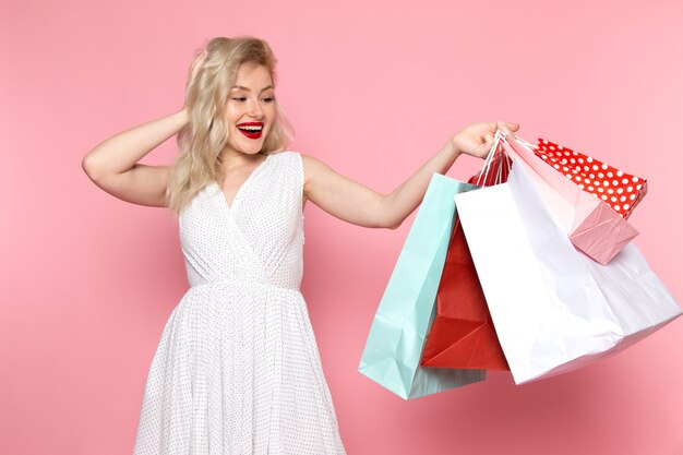 A front view young beautiful lady in white dress holding shopping packages with smile on her face