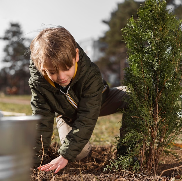 Free photo front view of young boy planting a tree outdoors