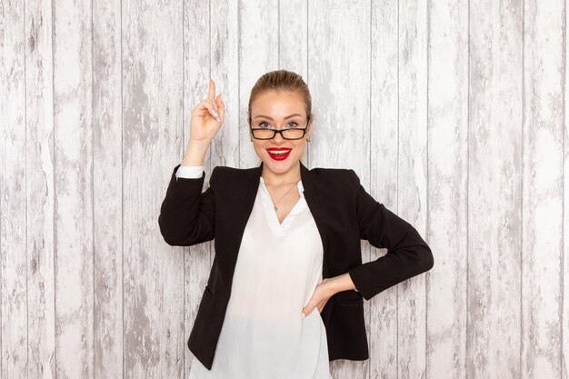 Front view young businesswoman in strict clothes black jacket with optical sunglasses smiling on white desk work job office business woman lady