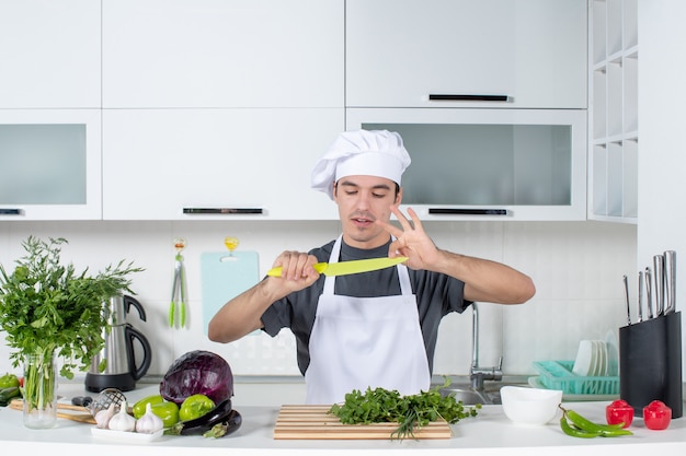 Front view young chef in uniform cleaning knife