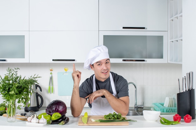 Front view young chef in uniform cutting greens on cutting board