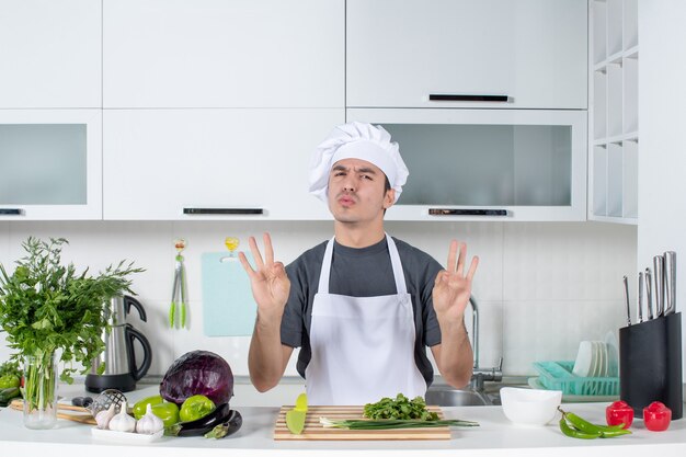 Front view young chef in uniform showing threee fingers