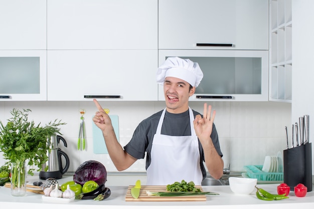 Front view young chef in uniform sticking out his tongue making okey sign