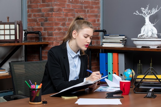 Free photo front view of young confident female assistant sitting at her desk and holding document in the office