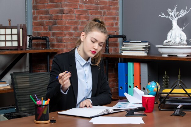 Front view of young confident female assistant sitting at her desk and reading document in the office