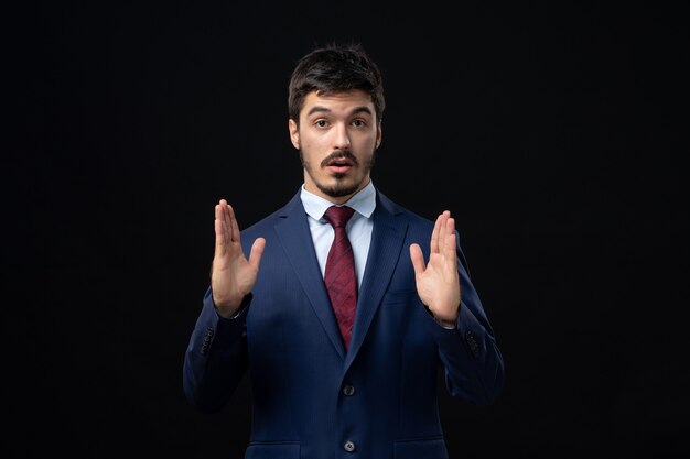 Front view of young and confused bearded man making sure something with suspicious glances on dark wall