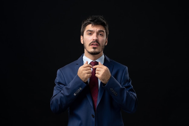 Front view of young confused bearded man posing on isolated dark wall