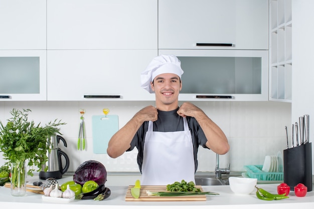 Front view young cook in uniform standing behind table