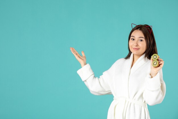 front view young female in bathrobe holding sliced kiwis on blue background