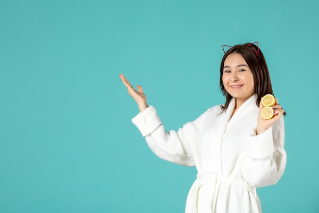 front view young female in bathrobe holding sliced lemons on blue background