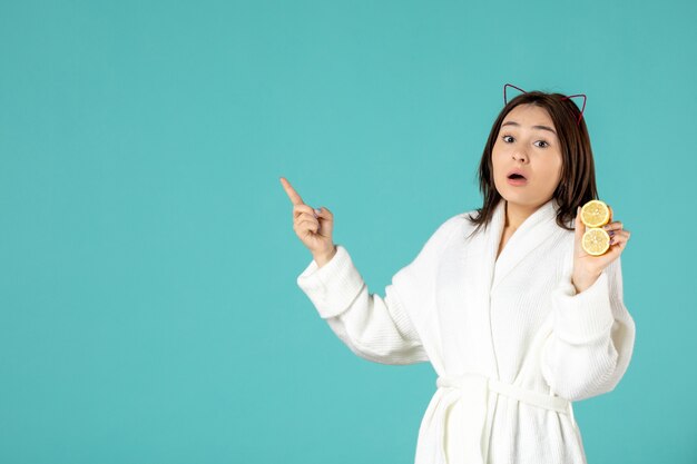 front view young female in bathrobe holding sliced lemons on blue background