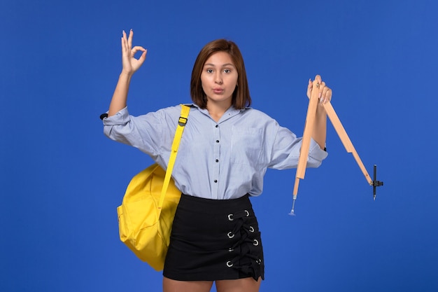 Front view of young female in blue shirt holding wooden figure on light-blue wall