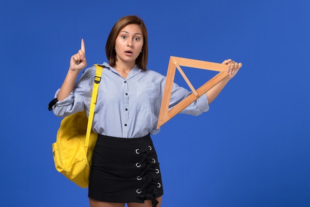 Front view of young female in blue shirt holding wooden triangle on blue wall