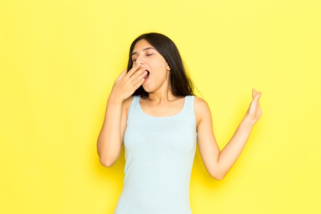 A front view young female in blue shirt posing and sneezing on the yellow background girl pose model