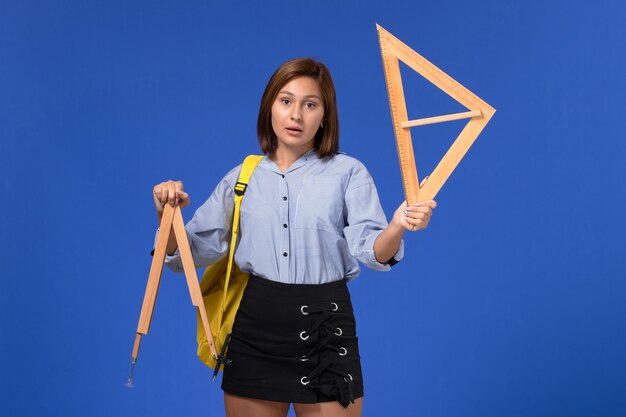 Front view of young female in blue shirt wearing yellow backpack holding wooden figures