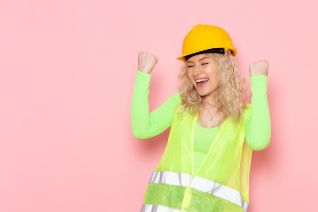 Free Photo front view young female builder in green construction suit helmet happy expression on the pink space architecture construction work