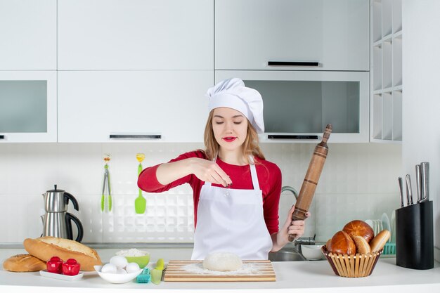 Front view young female cook sprinkling flour to dough on cutting board in the kitchen