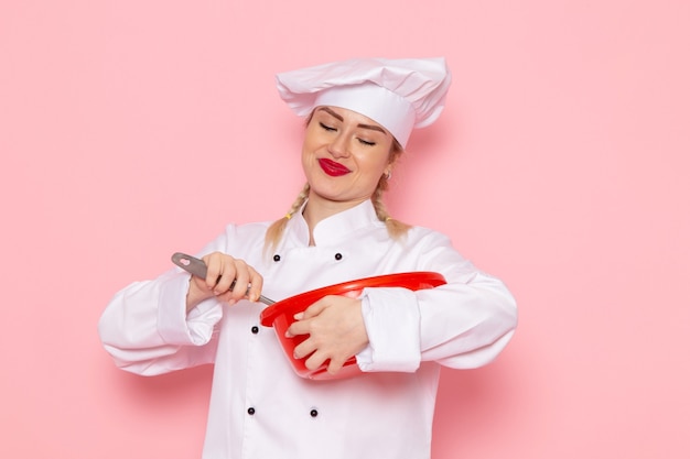 Free Photo front view young female cook in white cook suit mixing up red bowl on the pink space cook cuisine job work  photo