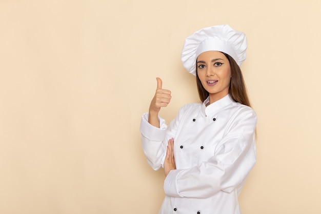 Front view of young female cook in white cook suit posing and smiling on light-white wall