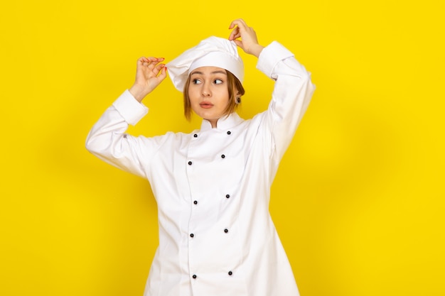 Free photo a front view young female cook in white cook suit and white cap fixing her suit on the yellow