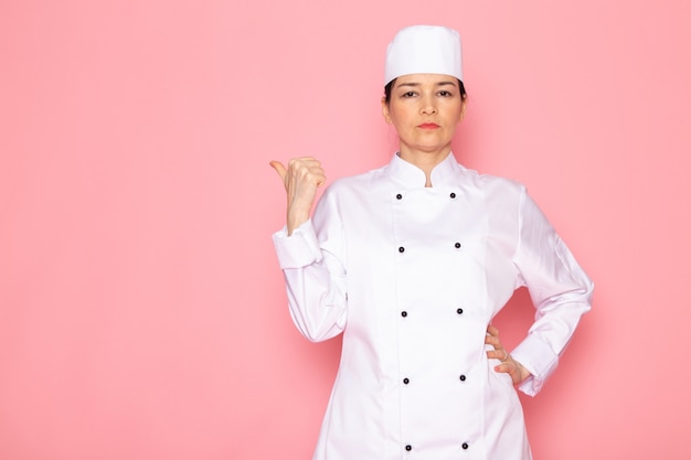 A front view young female cook in white cook suit white cap posing displeased serious look with hand expression