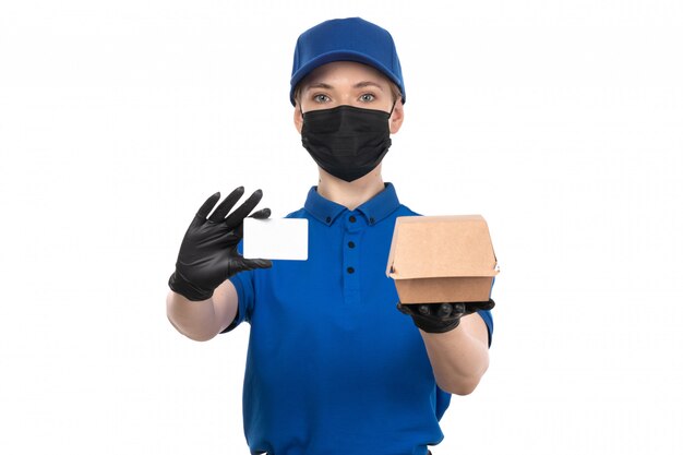 A front view young female courier in blue uniform black mask and gloves holding food delivery package