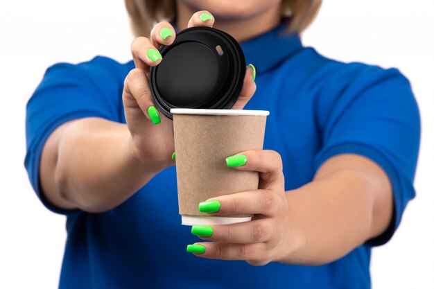 A front view young female courier in blue uniform holding coffee cup