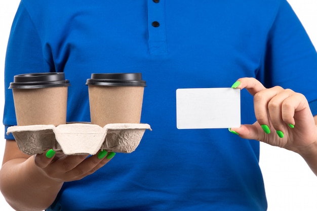 Free photo a front view young female courier in blue uniform holding coffee cups and white card