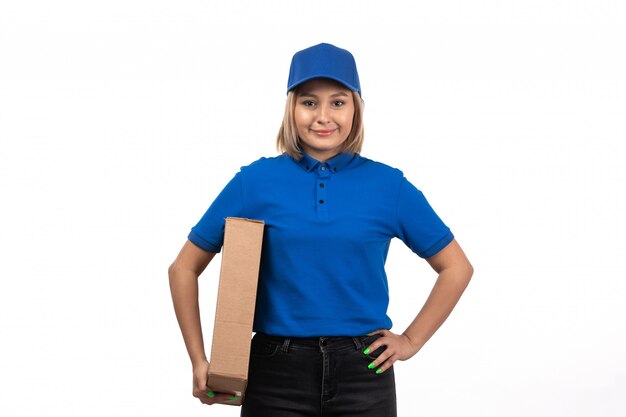 A front view young female courier in blue uniform holding food delivery package with smile on her face