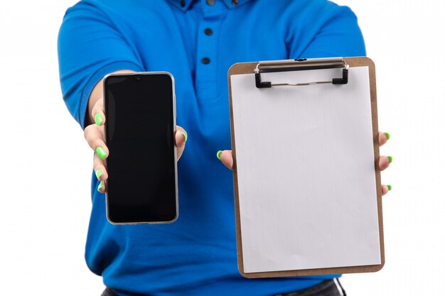 A front view young female courier in blue uniform holding phone and notepad