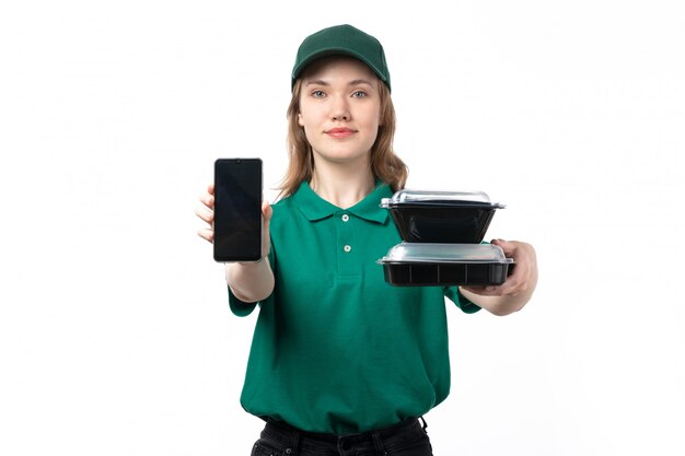 A front view young female courier in green uniform holding smartphone and bowls with food