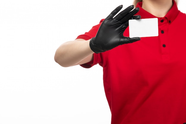 A front view young female courier in red shirt black leather gloves holding white card on the white background uniform service delivering