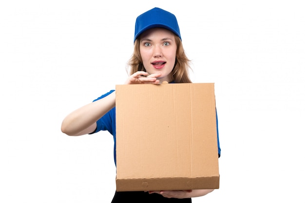 A front view young female courier in uniform holding delivery package and opening it with curious expression