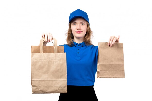 A front view young female courier in uniform holding delivery packages smiling