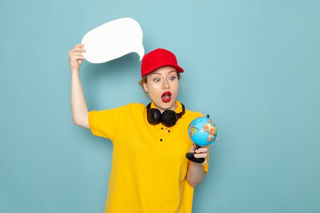 Free Photo front view young female courier in yellow shirt and red cape holding little globe and white sign on the blue space work   