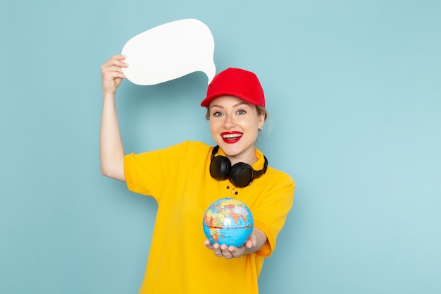 Free photo front view young female courier in yellow shirt and red cape holding little globe and white sign with smile on the blue space