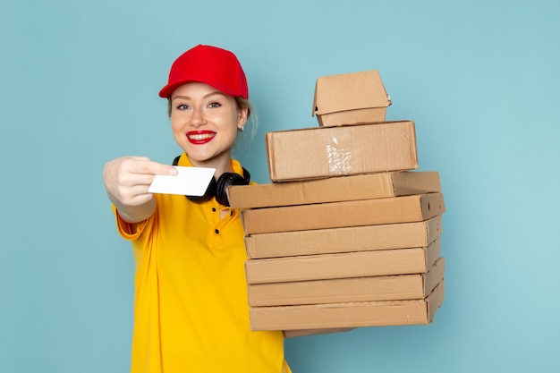 Free Photo front view young female courier in yellow shirt and red cape holding multiply  packages and white card on the blue space   job