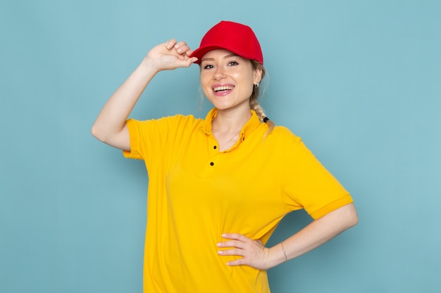 Free Photo front view young female courier in yellow shirt and red cape smiling and posing on the blue space   job work girl