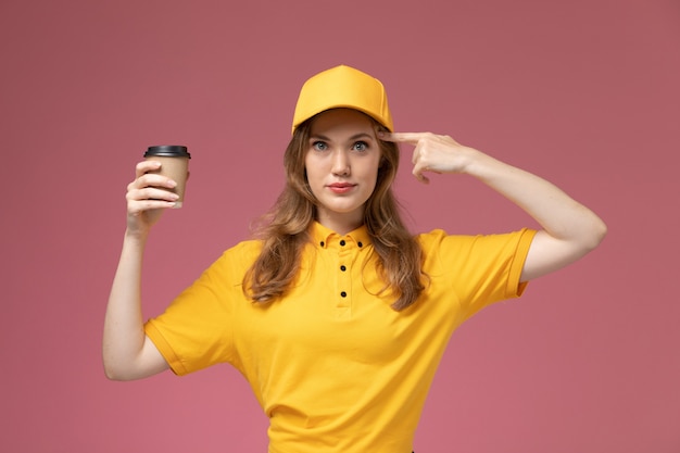 Free Photo front view young female courier in yellow uniform holding delivery coffee and posing on the pink background job uniform delivery service worker