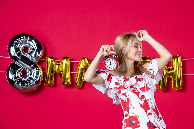 Free photo front view young female in cute dress holding clock on red color