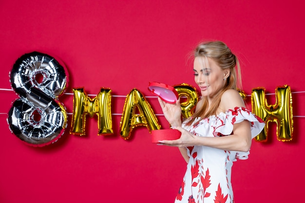 Free photo front view young female in cute dress holding and opening present on decorated red beauty womens day color