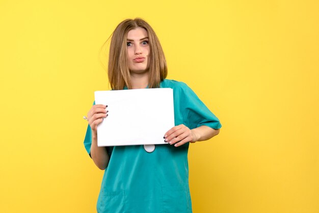 Front view of young female doctor holding files on yellow wall