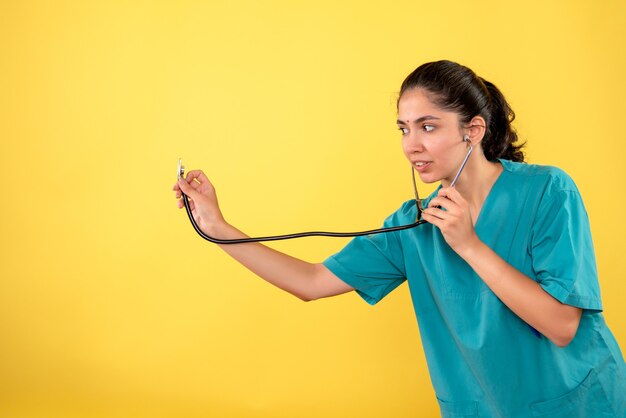 Front view of young female doctor holding stethoscope on yellow wall