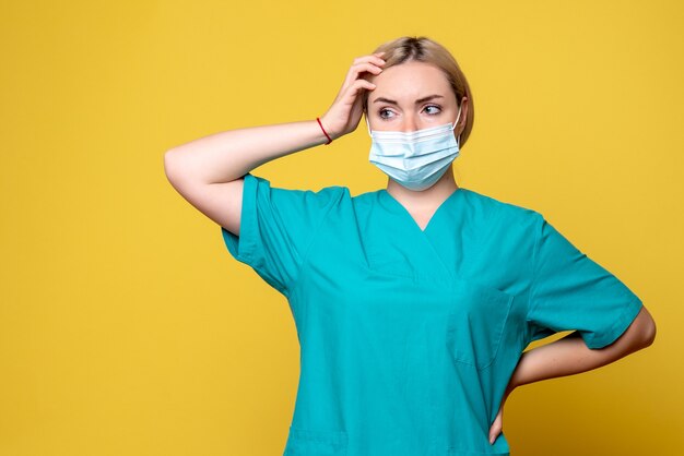 Front view of young female doctor in medical shirt and mask on yellow wall