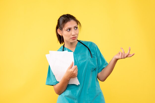 Front view young female doctor in medical shirt with papers on yellow background