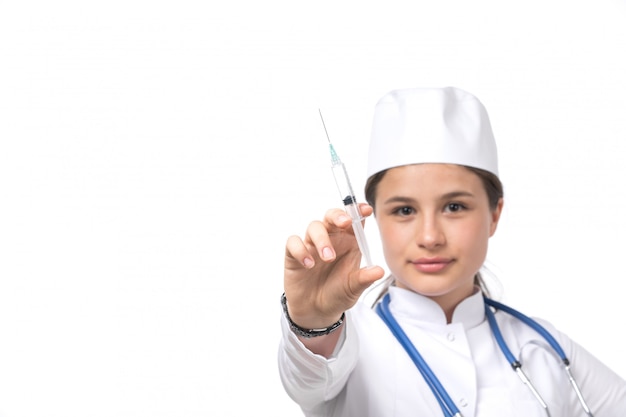 A front view young female doctor in white medical suit and white cap with blue stethoscope holding injection 