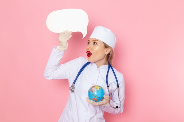 Free photo front view young female doctor in white medical suit with blue stethoscope holding little globe on the pink space medicine medical hospital health