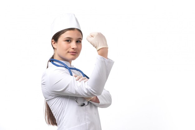 A front view young female doctor in white medical suit with blue stethoscope wearing gloves and flexing 