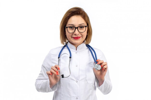 A front view young female doctor in white medical suit with stethoscope smiling on the white