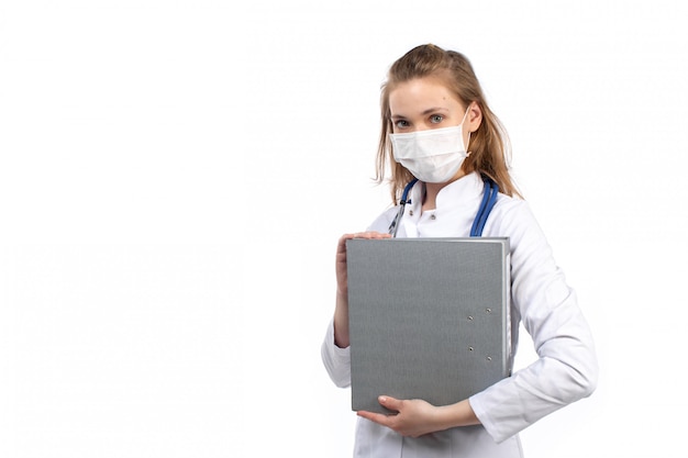 Free photo a front view young female doctor in white medical suit with stethoscope wearing white protective mask holding grey files on the white